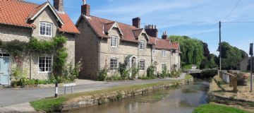 Limestone cottages with red pan tile roof along the side of a Brookside at Hovingham - motorcbike tour Yorkshire and Lake District